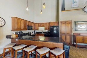 A kitchen with wooden cabinets, a black refrigerator, a large island with bar stools, and pendant lighting. - Ski-in/out condo with pool, hot tub - steps to Snowflake Lift (Breckenridge)