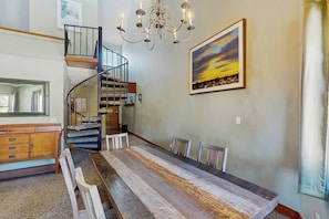 A dining area with a long wooden table, chairs, a chandelier, a staircase, and a painting on the wall. - Ski-in/out condo with pool, hot tub - steps to Snowflake Lift (Breckenridge)
