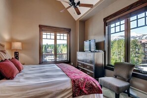 Une chambre à coucher comprenant un lit, une commode, une chaise, un ventilateur de plafond et de grandes fenêtres donnant sur la montagne.