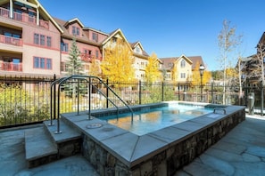 A swimming pool with a stone border, surrounded by a metal fence, and adjacent to multi-story buildings with balconies. - Bright, luxury condo with pool, hot tubs & gym - walk to lifts & downtown (Breckenridge)