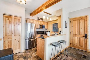 Eine Küche mit Holzausstattung, einem Edelstahlkühlschrank, einer Mikrowelle, einem Spülbecken und einem Barhocker.