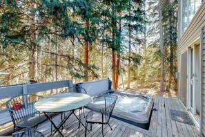 Eine Holzterrasse mit Whirlpool, zwei Metallstühlen und einem Tisch.