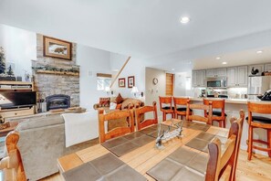 Ein Wohnzimmer mit Kamin, ein Essbereich mit Holzkästen, eine Küche mit modernen Geräten und ein Fernseher.