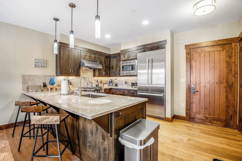 Una cocina con una isla grande, electrodomésticos de acero inoxidable, gabinetes de madera y taburetes de bar.