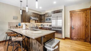 A kitchen with a large island, stainless steel appliances, wooden cabinets, and bar stools. - Walk-to-lift condo with beautiful view, outdoor pool, hot tubs & fitness center (Breckenridge)