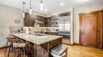Una cocina con una isla grande, electrodomésticos de acero inoxidable, gabinetes de madera y taburetes de bar.