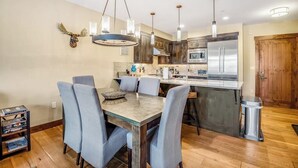 A modern kitchen with a central island, stainless steel appliances, and a dining area with blue chairs. - Walk-to-lift condo with beautiful view, outdoor pool, hot tubs & fitness center (Breckenridge)