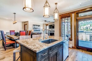 A modern kitchen with a large island, pendant lighting, and a view to the outside. - Light-filled corner condo with great view, pool & hot tubs - walk to lifts (Breckenridge)