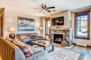 A living room with a sofa, coffee table, fireplace, television, and artwork. - Light-filled corner condo with great view, pool & hot tubs - walk to lifts (Breckenridge)