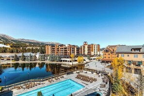 A hotel with a swimming pool, a mountain backdrop, and a clear sky. - Light-filled corner condo with great view, pool & hot tubs - walk to lifts (Breckenridge)
