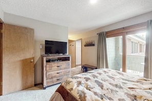 A bedroom with a bed, a wooden dresser, a television, and a sliding glass door leading to a balcony. - Condo in the heart of town with balcony, steps to the slopes and Main Street (Breckenridge)