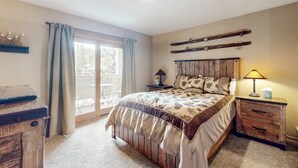 Ein Schlafzimmer mit Bett, Schminktisch, Nachttisch, Lampe und einem Fenster mit Vorhängen.
