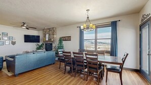A living room with a fireplace, a dining table with chairs, a sofa, a TV, and a ceiling fan. - Mountain getaway with hot tub, game room, fireplace, and modern interior (Granby)