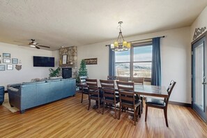 Una sala de estar con chimenea, una mesa de comedor con sillas, un sofá, un televisor y un ventilador de techo.