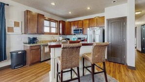 A kitchen with wooden cabinets, a microwave, a refrigerator, and two wicker bar stools. - Mountain getaway with hot tub, game room, fireplace, and modern interior (Granby)