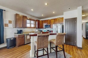 A kitchen with wooden cabinets, a microwave, a refrigerator, and two wicker bar stools. - Mountain getaway with hot tub, game room, fireplace, and modern interior (Granby)