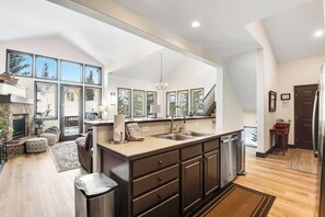 A modern kitchen with a large island, a dining area with a view, and a staircase leading to another level. - Bright mountain home with hot tub & fireplace, close to skiing & downtown (Breckenridge)