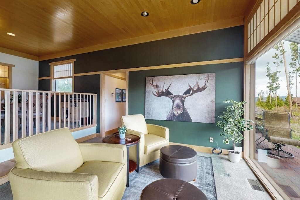 A modern interior with a large window, a sofa, a round ottoman, and a painting of a deer.