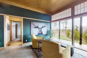 A room with a large window, a painting of a deer, and a yellow chair. - Cozy home with full kitchen, private patio & mountain views (Grand Lake)