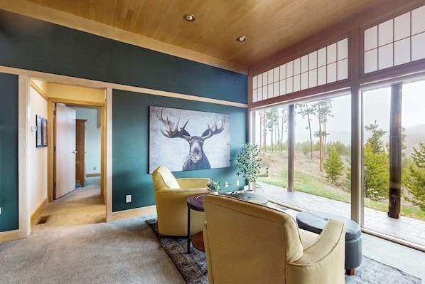A room with a large window, a painting of a deer, and a yellow chair. - Cozy home with full kitchen, private patio & mountain views (Grand Lake)