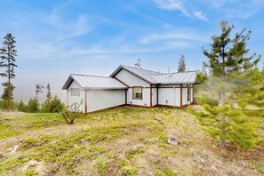 A two-story house with a sloped roof, a small porch, and a fenced yard. - Cozy home with full kitchen, private patio & mountain views (Grand Lake)