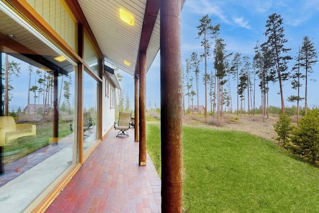 A covered outdoor area with a brick floor, large windows, and a view of a forest.