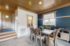 A dining area with a wooden table and chairs, a window with blinds, and a built-in bookshelf. - Cozy home with full kitchen, private patio & mountain views (Grand Lake)