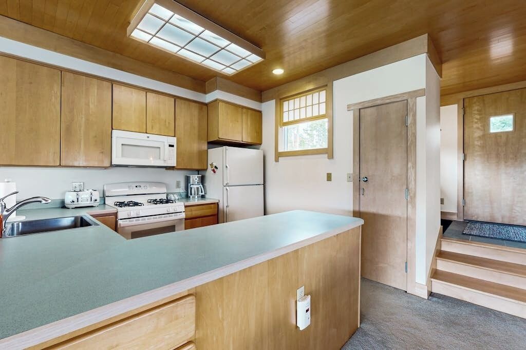 A compact kitchen with wooden cabinets, a microwave, a stove, and a refrigerator.