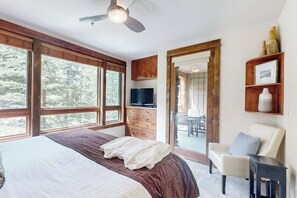 Une chambre à coucher avec un lit, un téléviseur, des armoires en bois, un ventilateur de plafond et de grandes fenêtres.