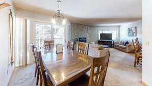A dining area with a wooden table and chairs, a living room with a sofa and TV, and a fireplace. - Comfy Ski-In Condo w/ Shared Hot Tub & Gas Fireplace - Close to the Mountain (Breckenridge)