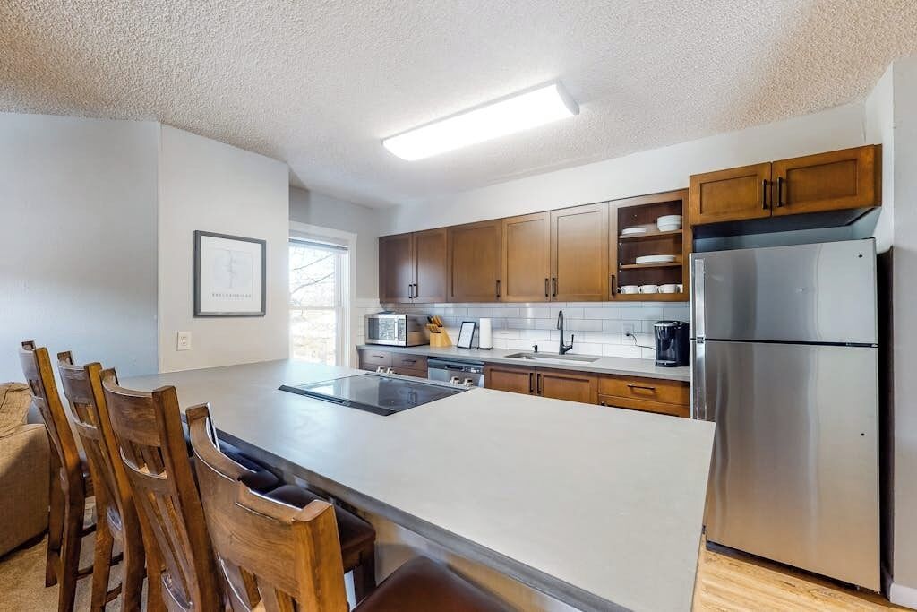 Una cocina moderna con una isla central, armarios de madera, electrodomésticos de acero inoxidable y un comedor con sillas de madera.