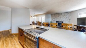 A spacious kitchen with a large island, wooden chairs, and a stone accent wall. - Comfy Ski-In Condo w/ Shared Hot Tub & Gas Fireplace - Close to the Mountain (Breckenridge)