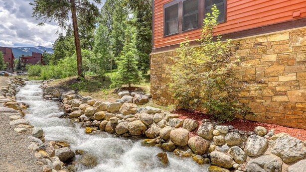 A stream flowing through a rocky bed, surrounded by trees and a red building with stone walls. - Comfy Ski-In Condo w/ Shared Hot Tub & Gas Fireplace - Close to the Mountain (Breckenridge)