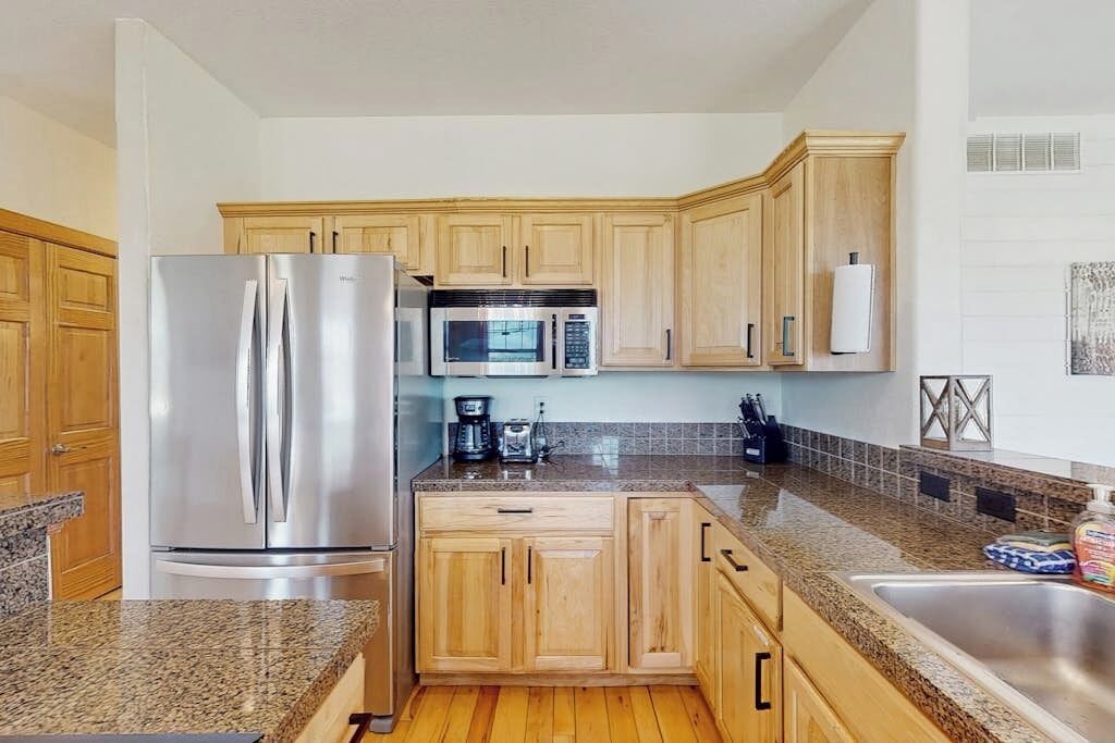 A kitchen with wooden cabinets, a stainless steel refrigerator, a microwave, and a granite countertop.