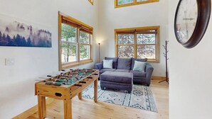 A living room with a foosball table, a sofa, and large windows. - Stunning house w/ mountain views, free WiFi, outdoor activities (Granby)