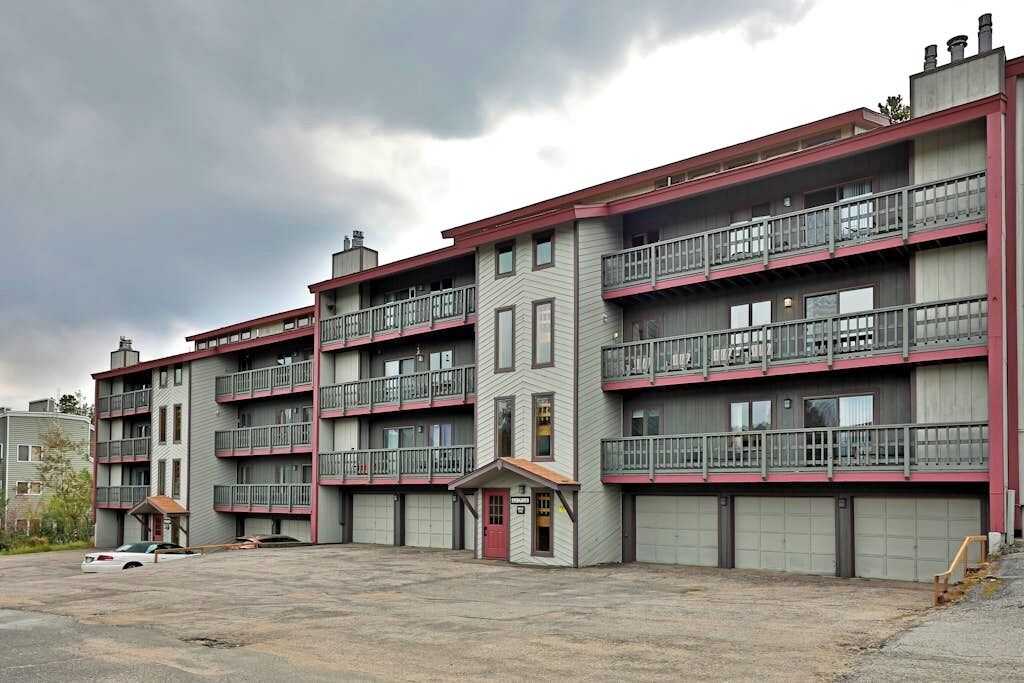 A multi-story apartment building with balconies, a small entrance, and a parking lot.