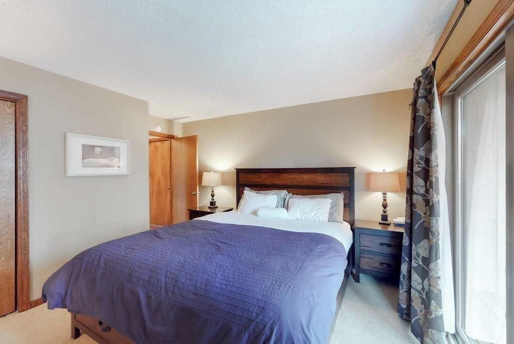 A bedroom with a bed, nightstands, a wooden wardrobe, and a window with curtains.