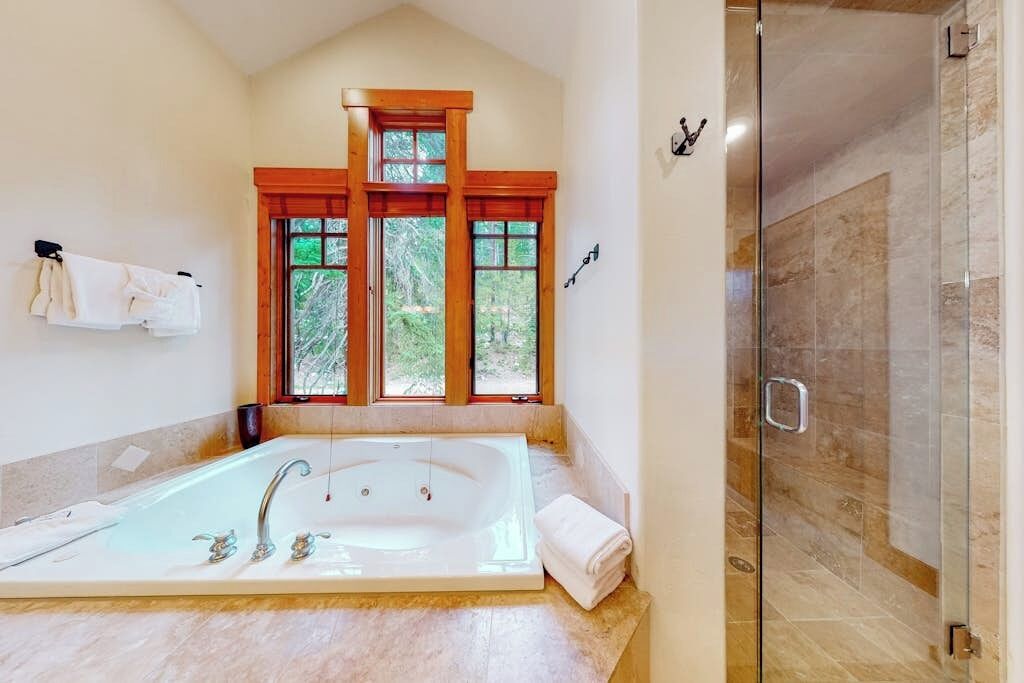 A bathroom with a large bathtub, a glass shower enclosure, and a window with wooden frames.