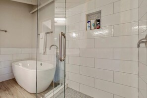 Un baño moderno con una bañera independiente, cabina de ducha con mampara de vidrio y un pequeño estante con artículos de aseo.
