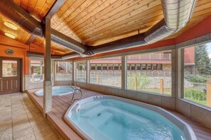 A spa area with two hot tubs, wooden ceiling, and large windows overlooking a fenced outdoor area. - Rustic mountain escape with fireplace, W/D, hot tub, & grill - near skiing (Breckenridge)