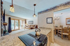 A kitchen with a stove, a kettle, a dining table with chairs, and a large window. - Rustic mountain escape with fireplace, W/D, hot tub, & grill - near skiing (Breckenridge)
