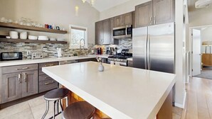 Een moderne keuken met een groot eiland, roestvrijstalen apparatuur en hanglampen.
