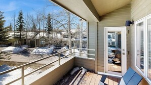 Een balkon met uitzicht op een besneeuwd landschap, een deur naar een overdekt terras en een klein zitgedeelte buiten.