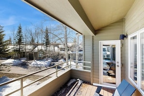 A balcony with a view of a snowy landscape, a door leading to a covered area, and a small outdoor seating area. - Renovated condo with deck, mountain view, fireplace & gorgeous kitchen (Crested Butte)