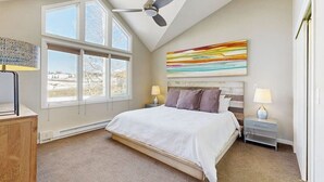 Een slaapkamer met een groot bed, twee nachtkastjes, een plafondventilator en een groot raam.