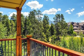Eine Holzdielen-Terrasse mit Geländer, umgeben von Bäumen und einem Berg im Hintergrund.