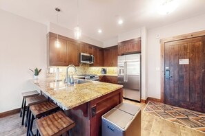 Eine Küche mit Granit-Arbeitsplatte, Edelstahlgeräten, Holzschränken und einem integrierten Mülleimer.