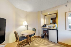 Ein gemütliches Hotelzimmer mit Esstisch, Stühlen, Fernseher, einer kleinen Küchenzeile und einem Spiegel.