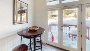 A room with a dining table, a bench, a framed picture on the wall, and a sliding glass door leading to a snowy outdoor area.