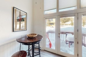 Une pièce comprenant une table à manger, un banc, un tableau encadré au mur et une porte-fenêtre coulissante donnant sur un espace extérieur enneigé.